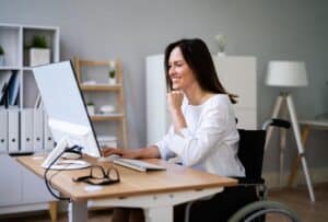 אישה נכה בכיסא גלגלים עובדת במחשב משרד נגיש – חיסכון בפטור אגרת רישוי עם תו נכה